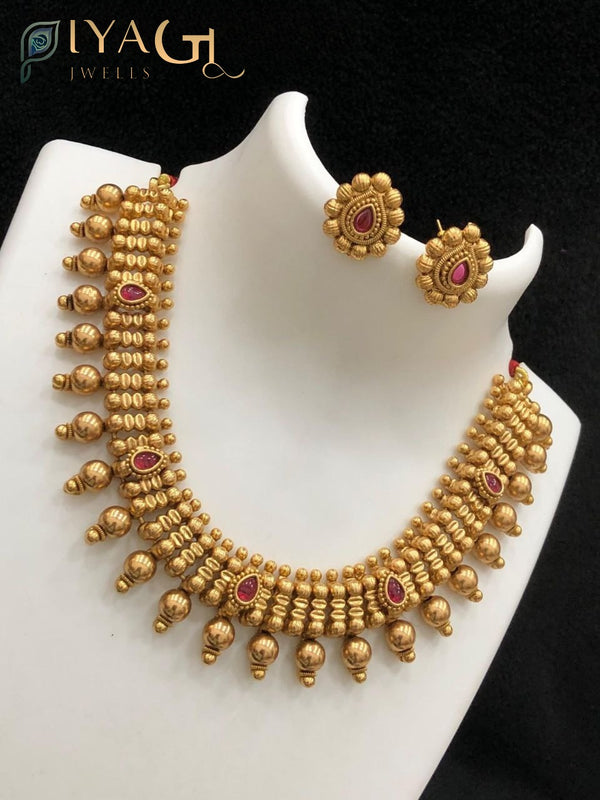 A woman wearing an antique polish brass metal necklace set with red kempu stones and matching earrings on a white bust. - PiyaGuJwells