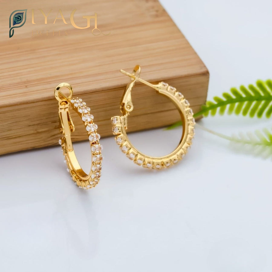 Gold colored hoop earrings with clear stones set in a pave style, resting on a wooden surface. - PiyaGuJwells
