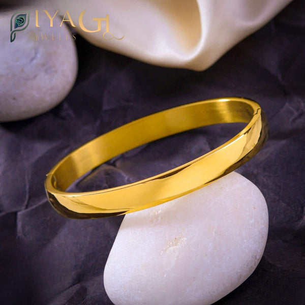Gold finish stainless steel bangle resting on a white stone background - PiyaGuJwells