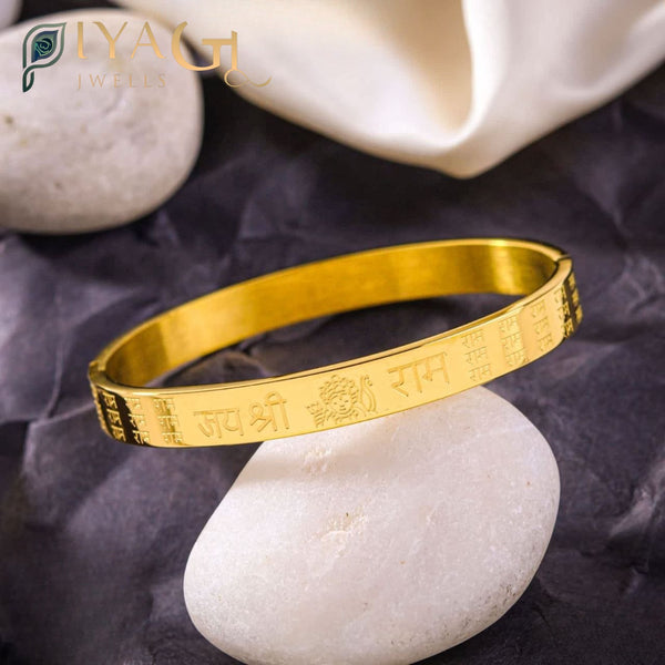Golden stainless steel bangle engraved with Jai Shri Ram text resting on a white stone. - PiyaGuJwells