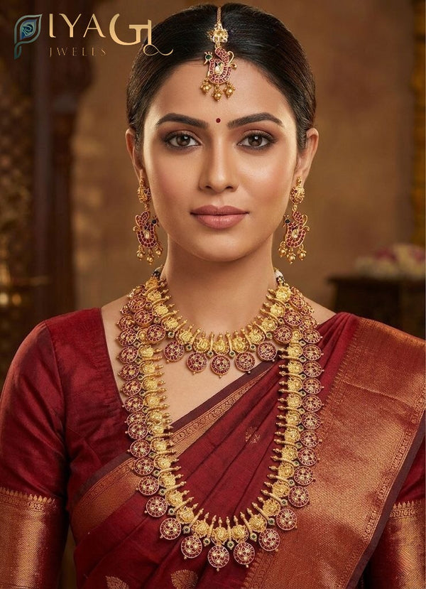 Woman wearing an antique finish brass metal jewelry set with red kempu stones, including a peacock maang tikka, long earrings, and a double-layered necklace. - PiyaGuJwells