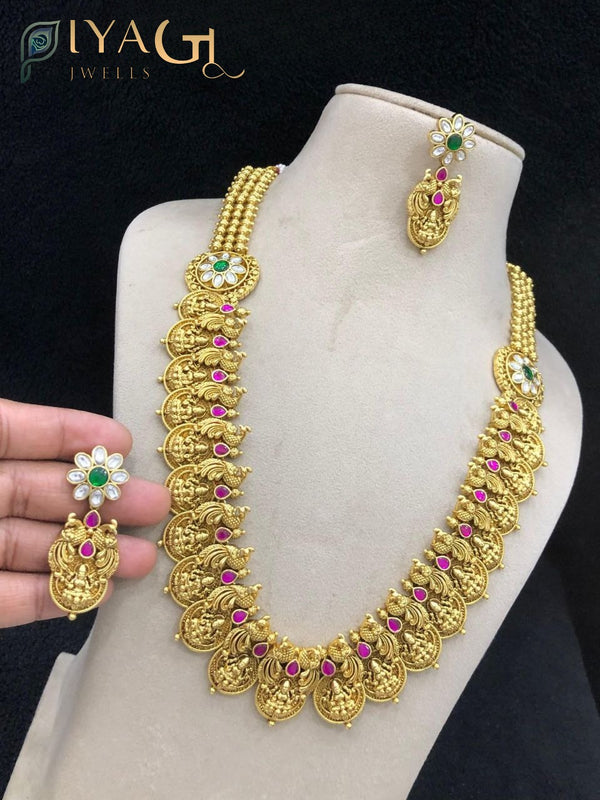 A woman wearing a traditional Indian imitation jewelry set consisting of an antique finish brass necklace with kundan stones and matching drop earrings. - PiyaGuJwells