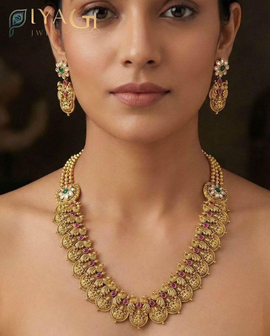 A woman wearing a traditional Indian imitation jewelry set consisting of an antique finish brass necklace with kundan stones and matching drop earrings. - PiyaGuJwells
