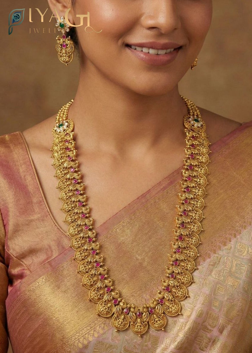 Woman wearing an antique gold finish long necklace with red and green stones, matching earrings, traditional Indian imitation jewelry set - PiyaGuJwells