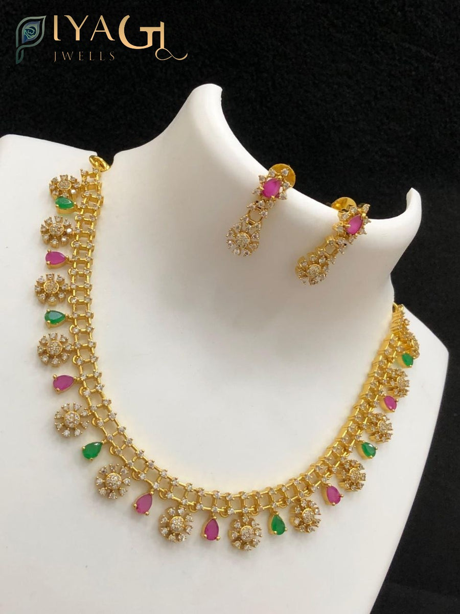 Gold-colored antique finish necklace set with pink and green imitation stones and matching earrings displayed on a bust. - PiyaGuJwells