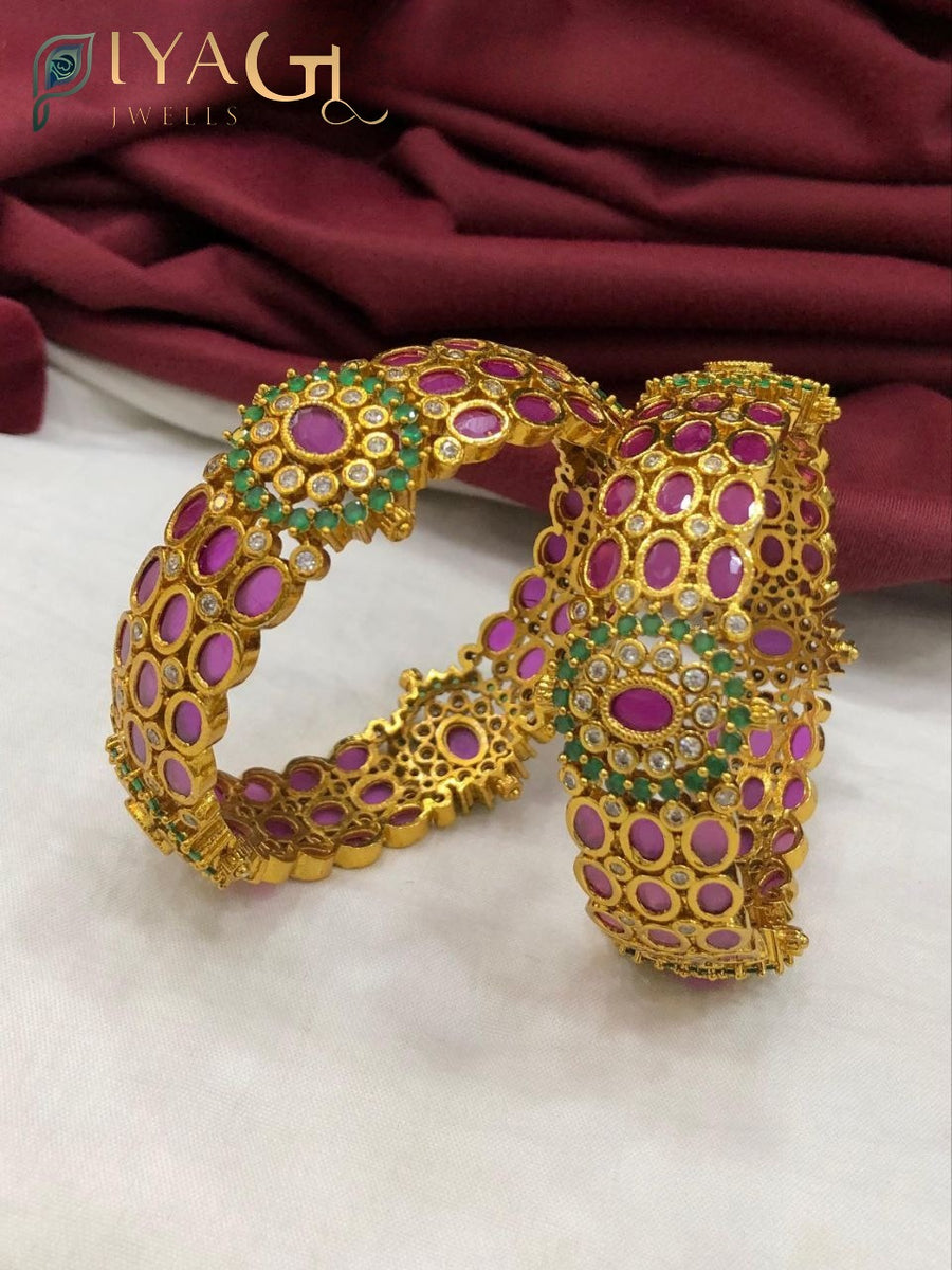 Two gold-tone bangle kaddas with purple stones and green accents on a white background. - PiyaGuJwells