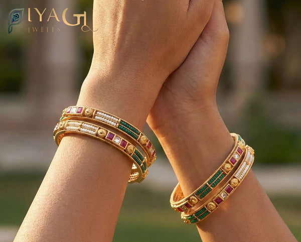 Hands displaying an antique finish brass bangle set with green and red stone accents. - PiyaGuJwells