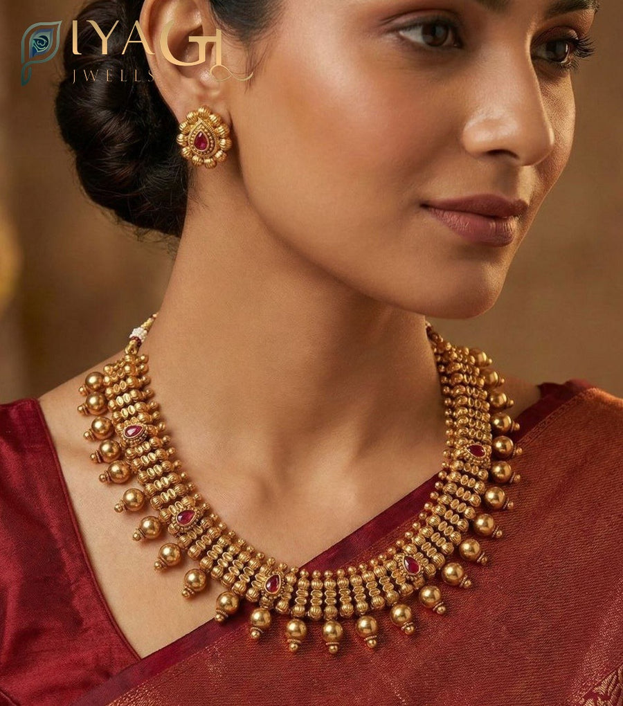A woman wearing an antique polish brass metal necklace set with red kempu stones and matching earrings on a white bust. - PiyaGuJwells