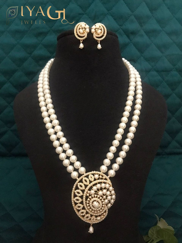 Imitation pearl mala set with large spiral pendant and matching earrings displayed on a black bust against a green background. - PiyaGuJwells