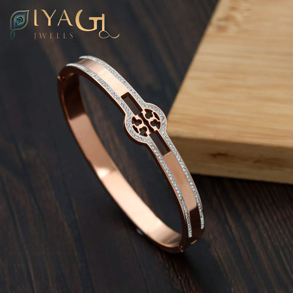 Rose gold stainless steel bangle with clover design and crystal accents on dark wood background - PiyaGuJwells